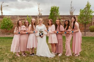 Bridal party in pink dresses poses together for group photo in garden setting.