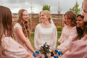 Bride and bridesmaids share intimate moment holding blue drinks during outdoor wedding celebration.