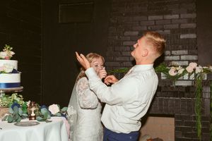 Playful moment of couple feeding each other wedding cake during reception.