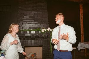 Couple laughing together during their wedding reception by a brick wall.