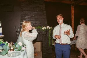 Couple shares drinks and laughter during wedding reception in rustic brick venue.