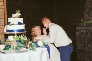 Couple shares playful moment while cutting their blue and white tiered wedding cake.