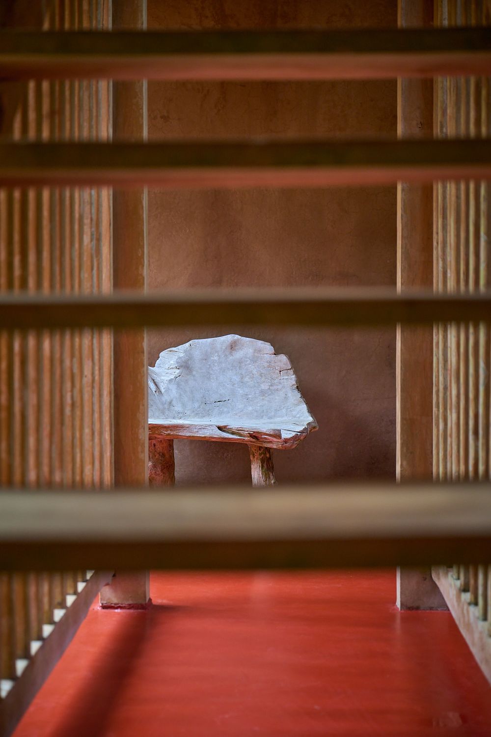A chunk of raw ice sits on a red surface, viewed through wooden slats in an artistic composition.