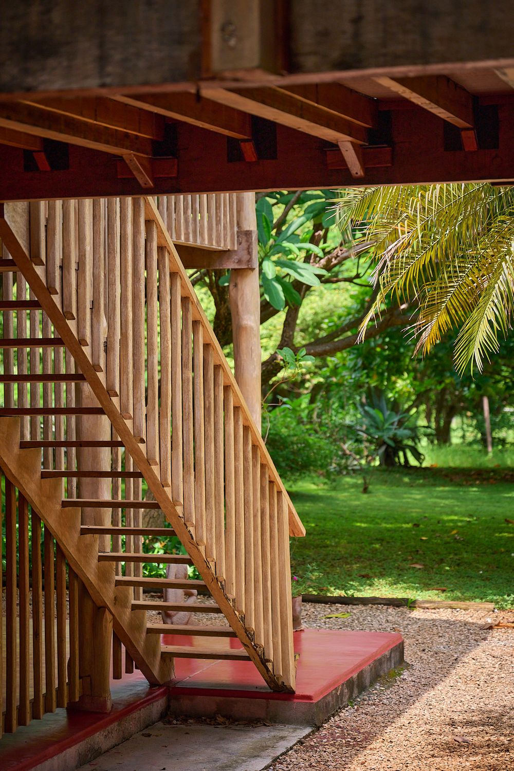 A wooden staircase with red cushioned bench seating underneath creates a cozy nook in a tropical garden setting.