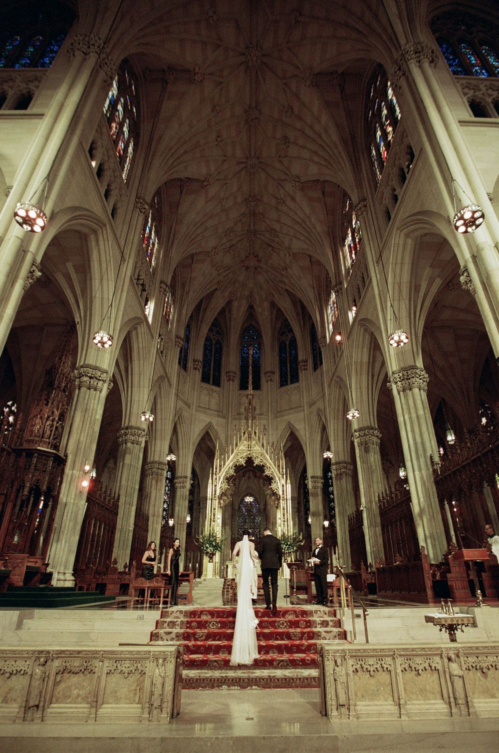 Couple at cathedral altar during wedding ceremony with Gothic arches and stained glass.