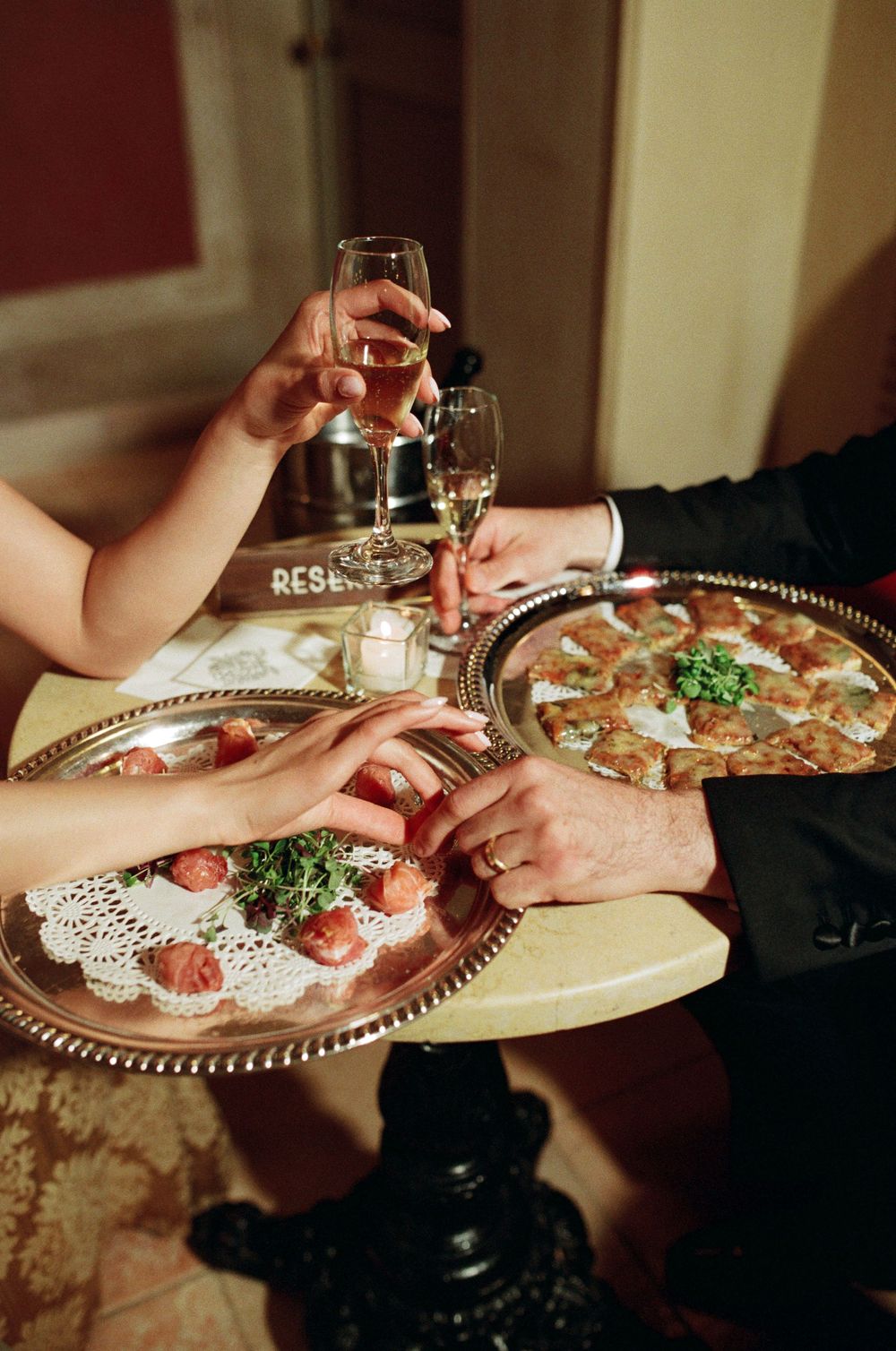 Couple toasts champagne over silver trays of elegant appetizers at a wedding reception table.
