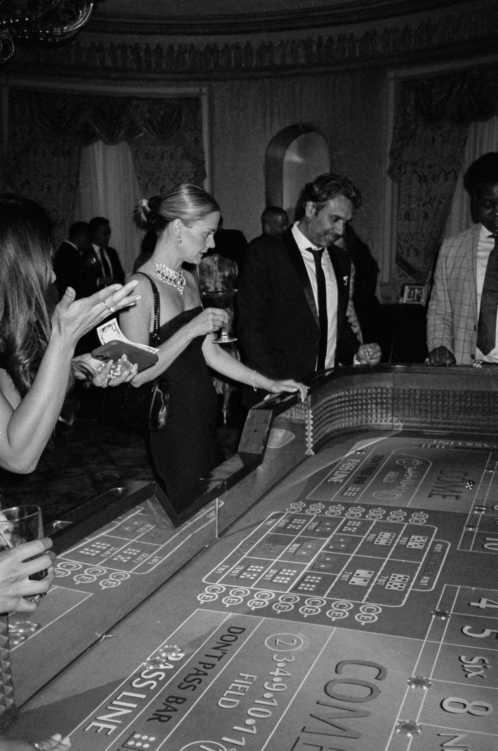 Guests in formal attire playing craps at a casino table during an elegant black tie event, black and white photo.