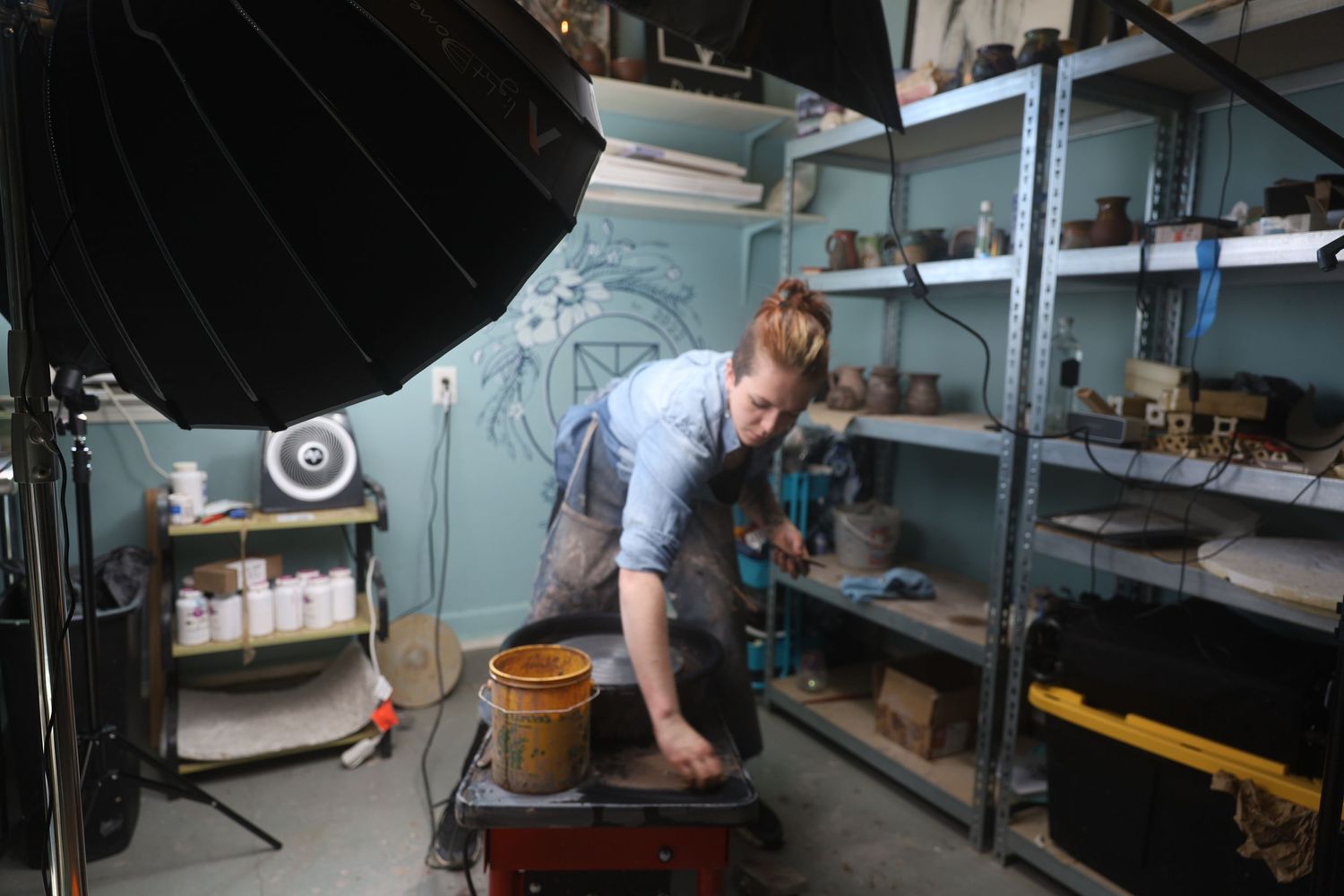 Potter working in a studio shaping clay on a pottery wheel to create handmade ceramic pieces.