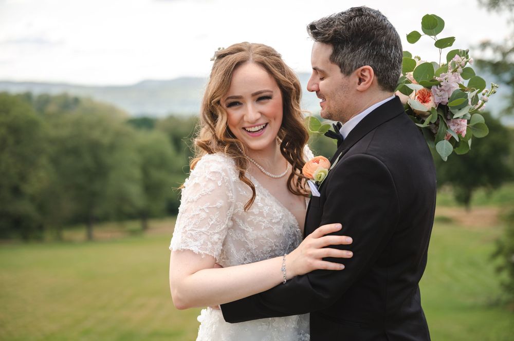 Joyful newlyweds embrace outdoors with rolling green hills in the background on their wedding day.