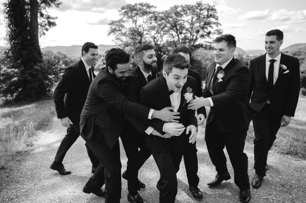 A group wearing black suits and ties walks together while playfully interacting on a scenic outdoor path.