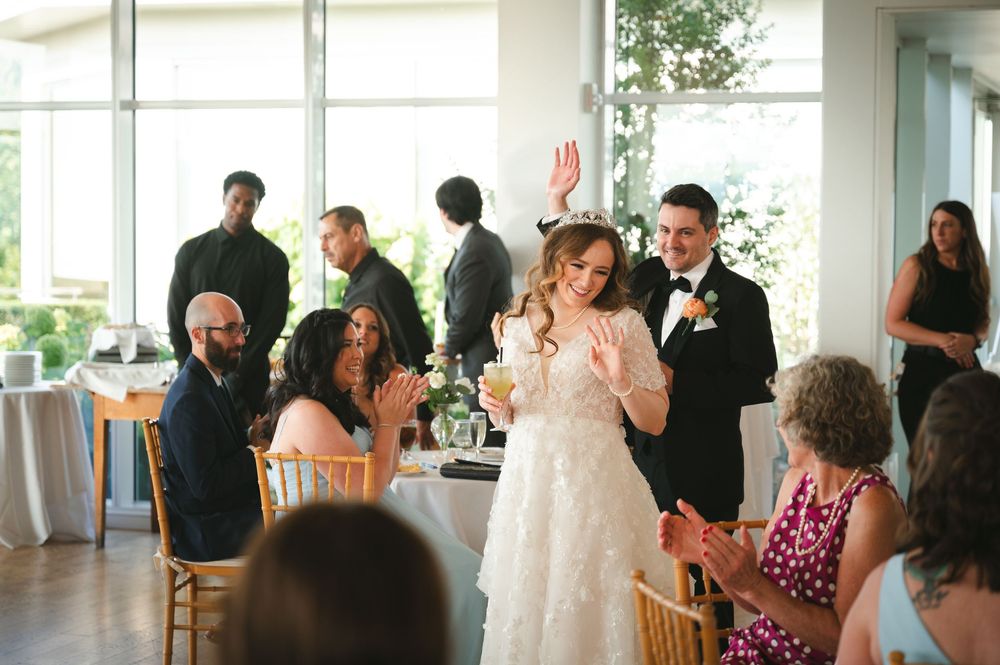Wedding reception with guests celebrating in a bright, window-filled venue with natural lighting.