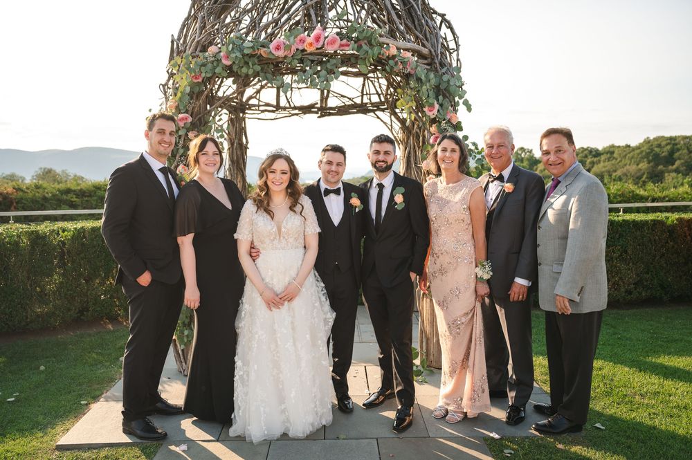 Wedding party poses together on a scenic lawn with mountain views and greenery in the background.