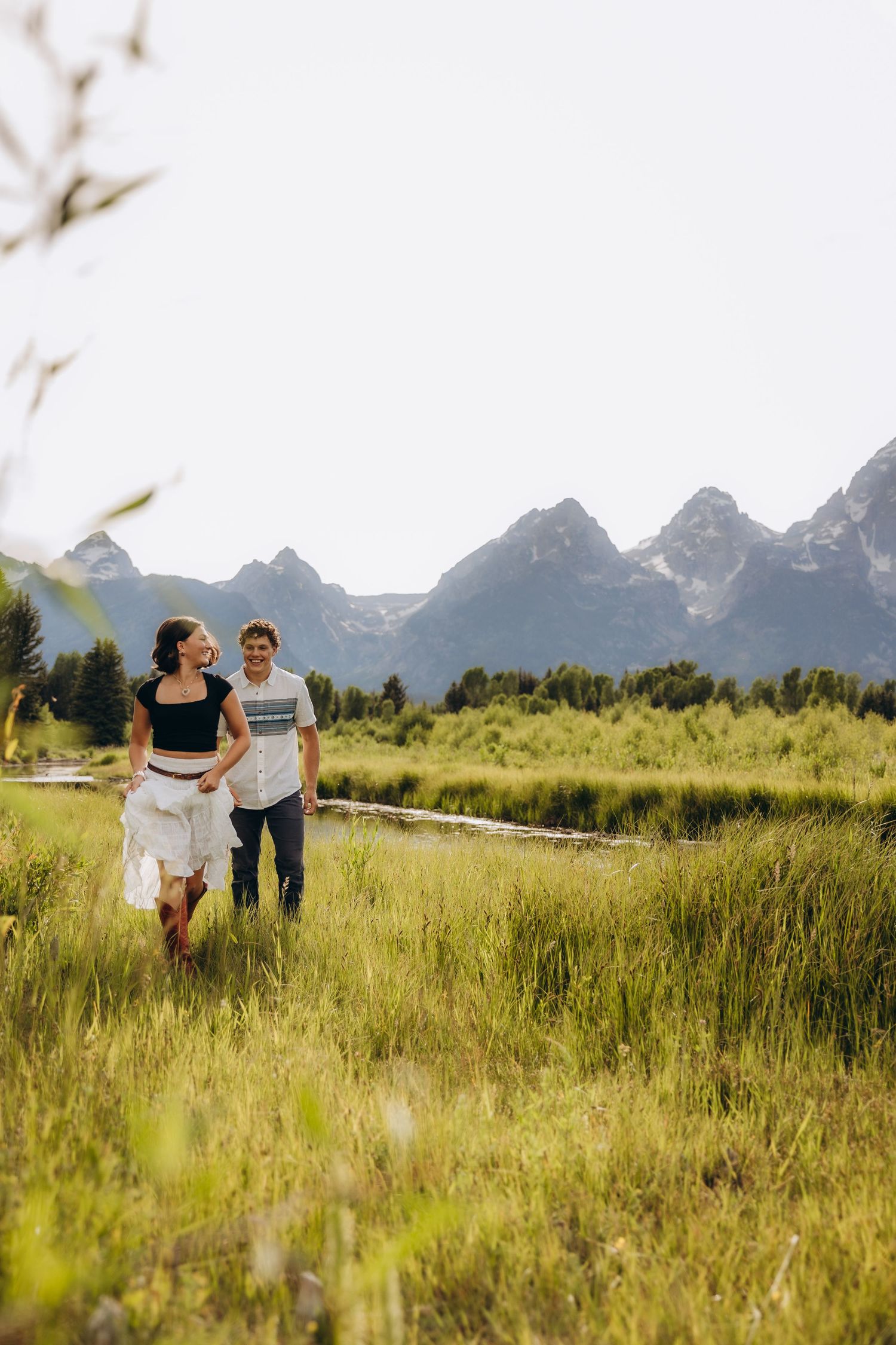 Two people walking together through a grassy meadow with majestic Grand Teton mountains rising in the background.