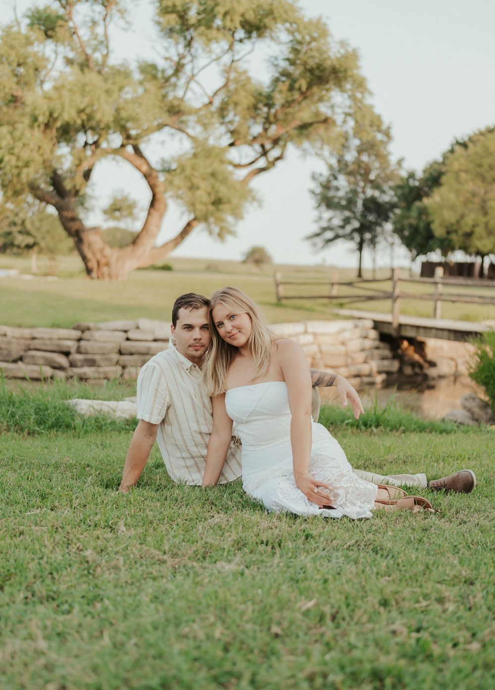 Relaxed engagement photo on grassy field with oak tree and country backdrop