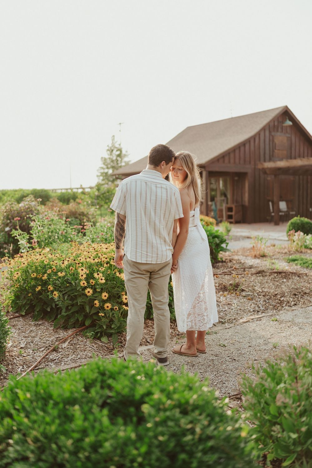 Sweet outdoor engagement photo in Kansas flower garden by rustic barn
