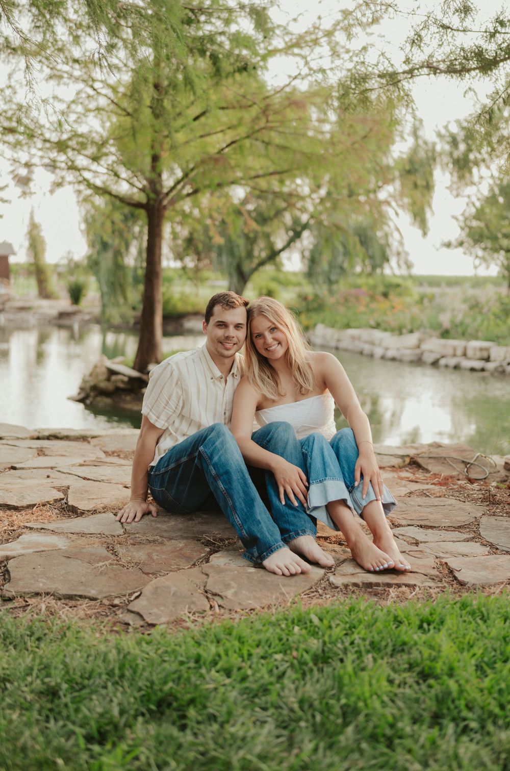 Peaceful couples portrait on stone by scenic pond and lush trees in Wichita