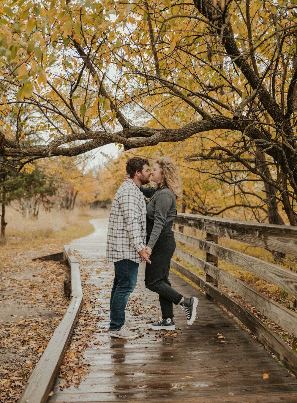Autumn engagement photo on wooden path under vibrant fall trees