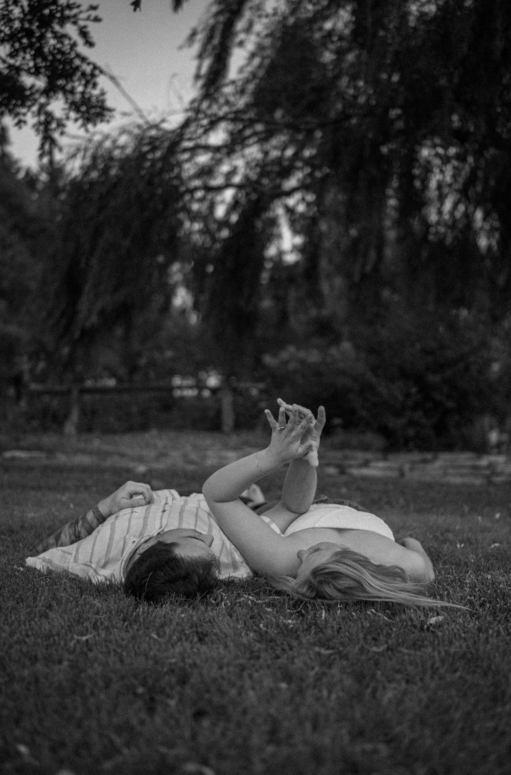 Candid black-and-white photo of couple laying under trees in quiet park