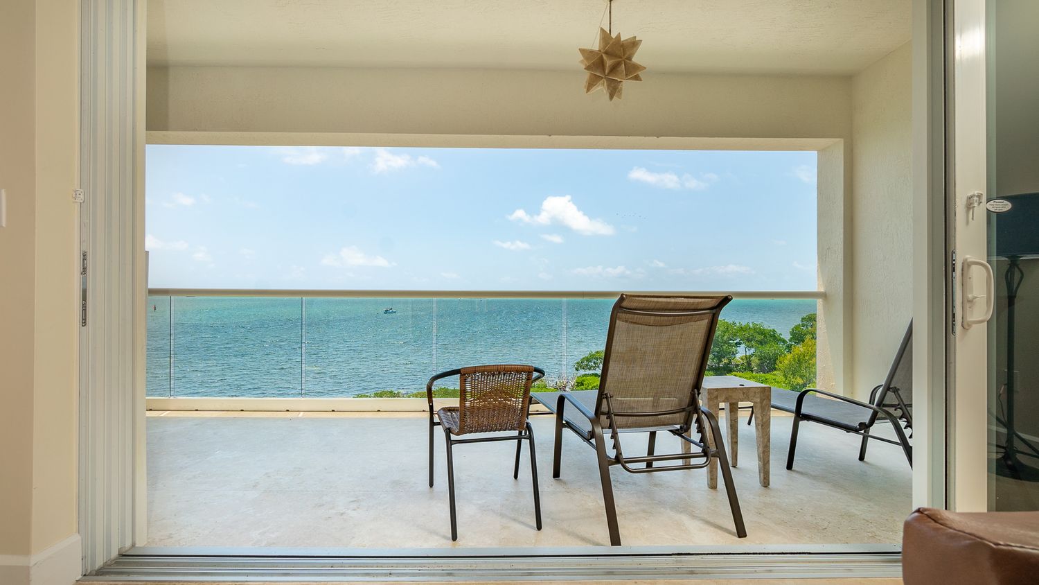 Ocean view through doorway with three patio chairs on balcony.