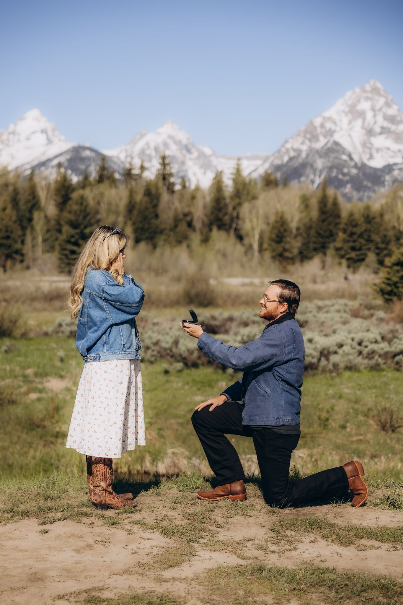 A couple gets engaged with a romantic proposal in Grand Teton National Park with snowy mountains in the background.