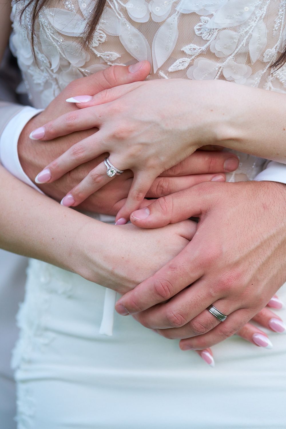 Close-up of newlyweds' hands showing wedding rings against lace dress.