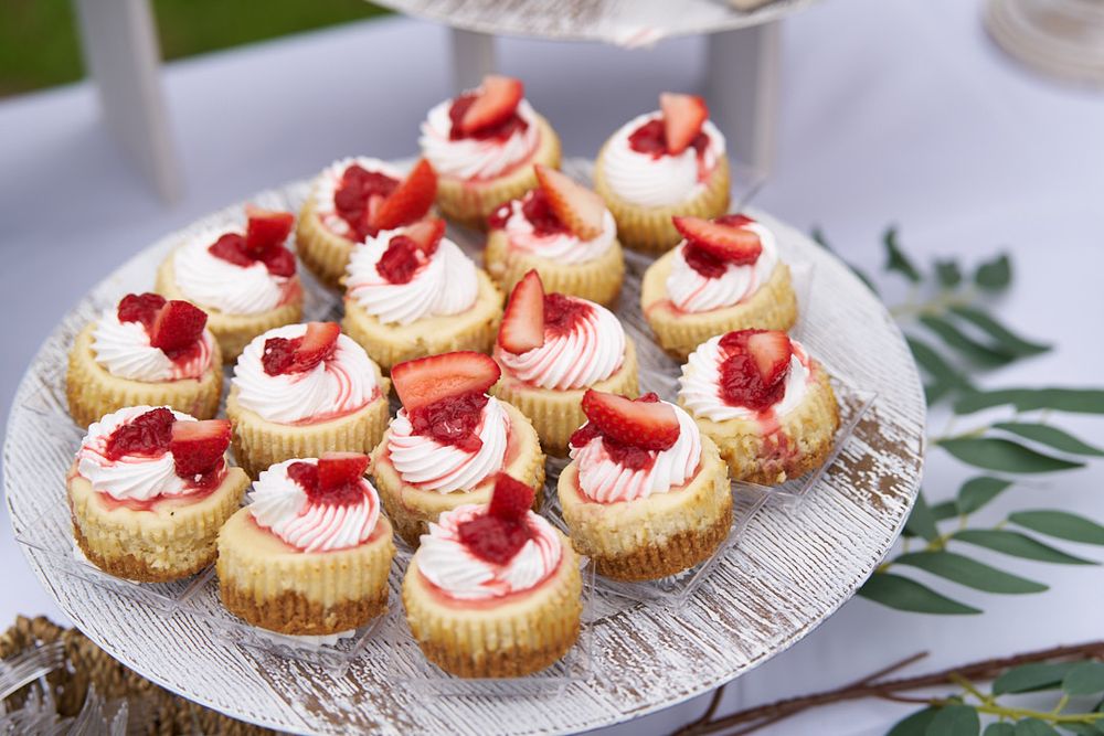 Mini vanilla cupcakes topped with pink frosting, fresh strawberries and powdered sugar on a decorative plate.