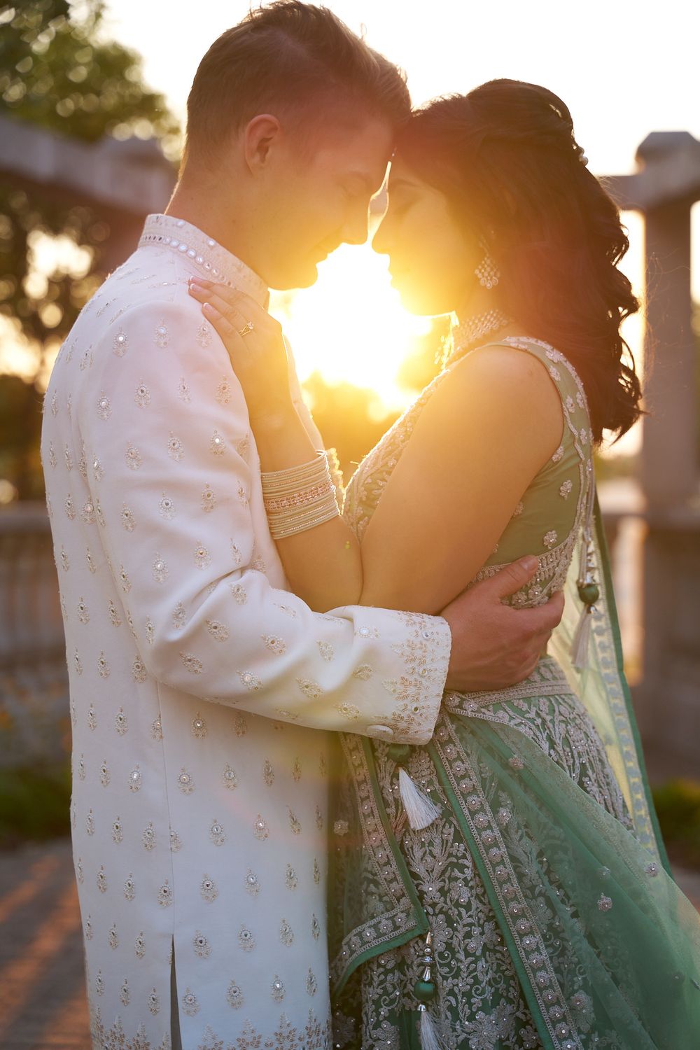 A couple embraces during golden hour sunset in elegant formal attire.