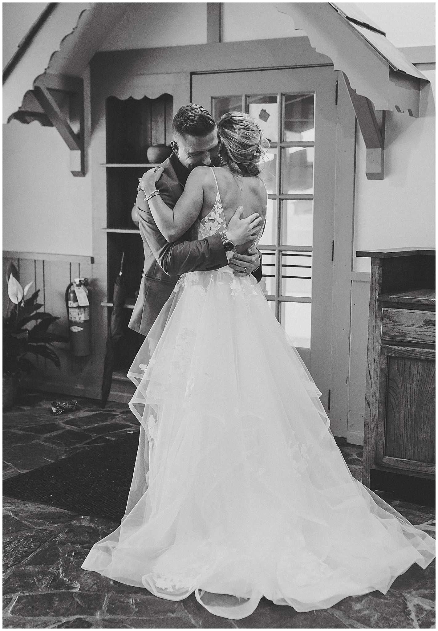 Black and white photo of couple embracing in elegant wedding attire in front of vintage building.