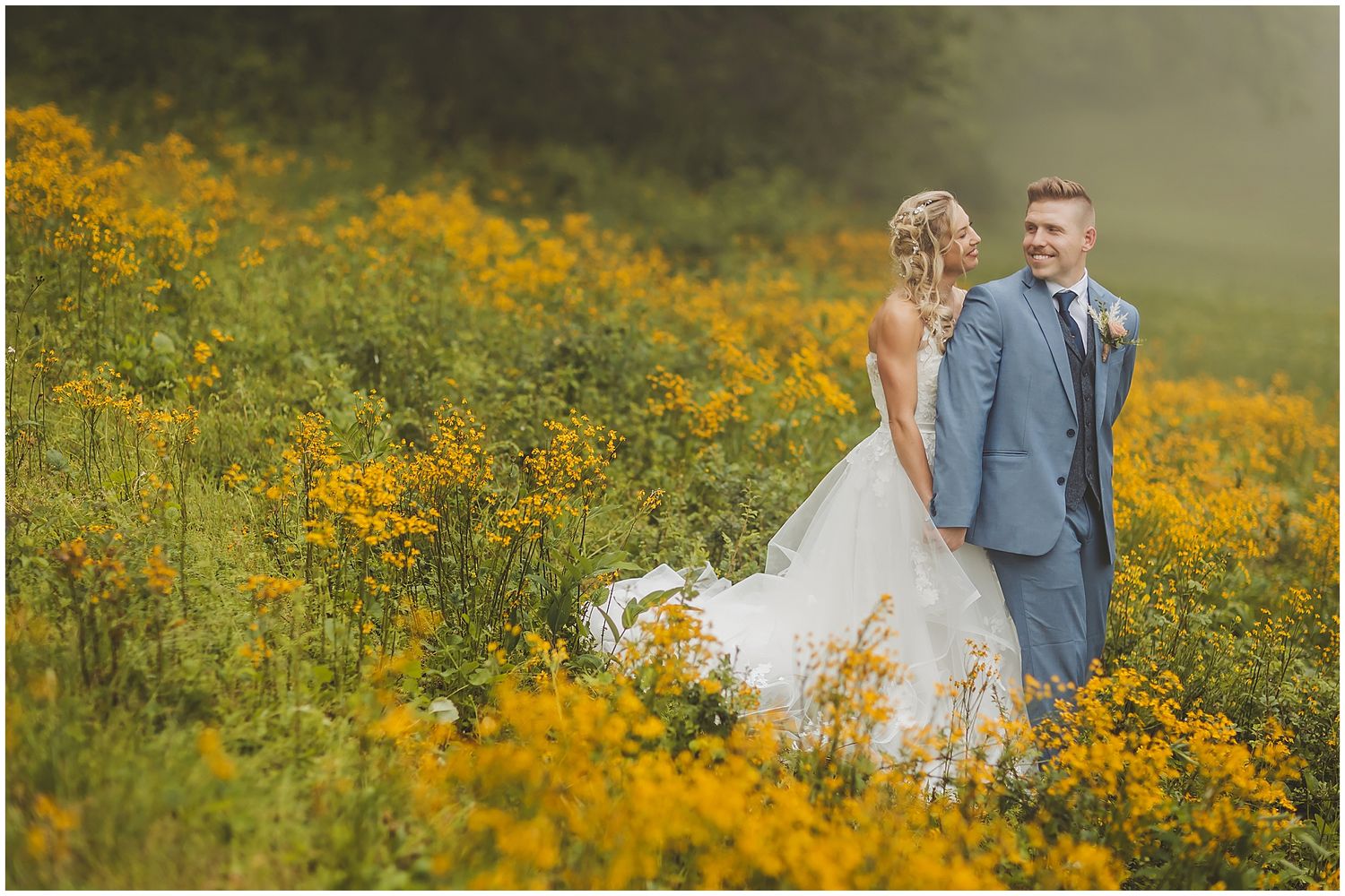 Wedding couple poses in field of vibrant yellow wildflowers on their special day.
