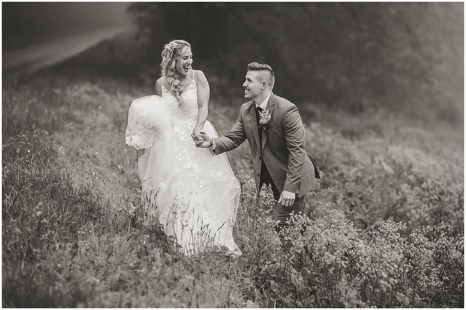 Black and white wedding portrait of couple walking through wildflower field.