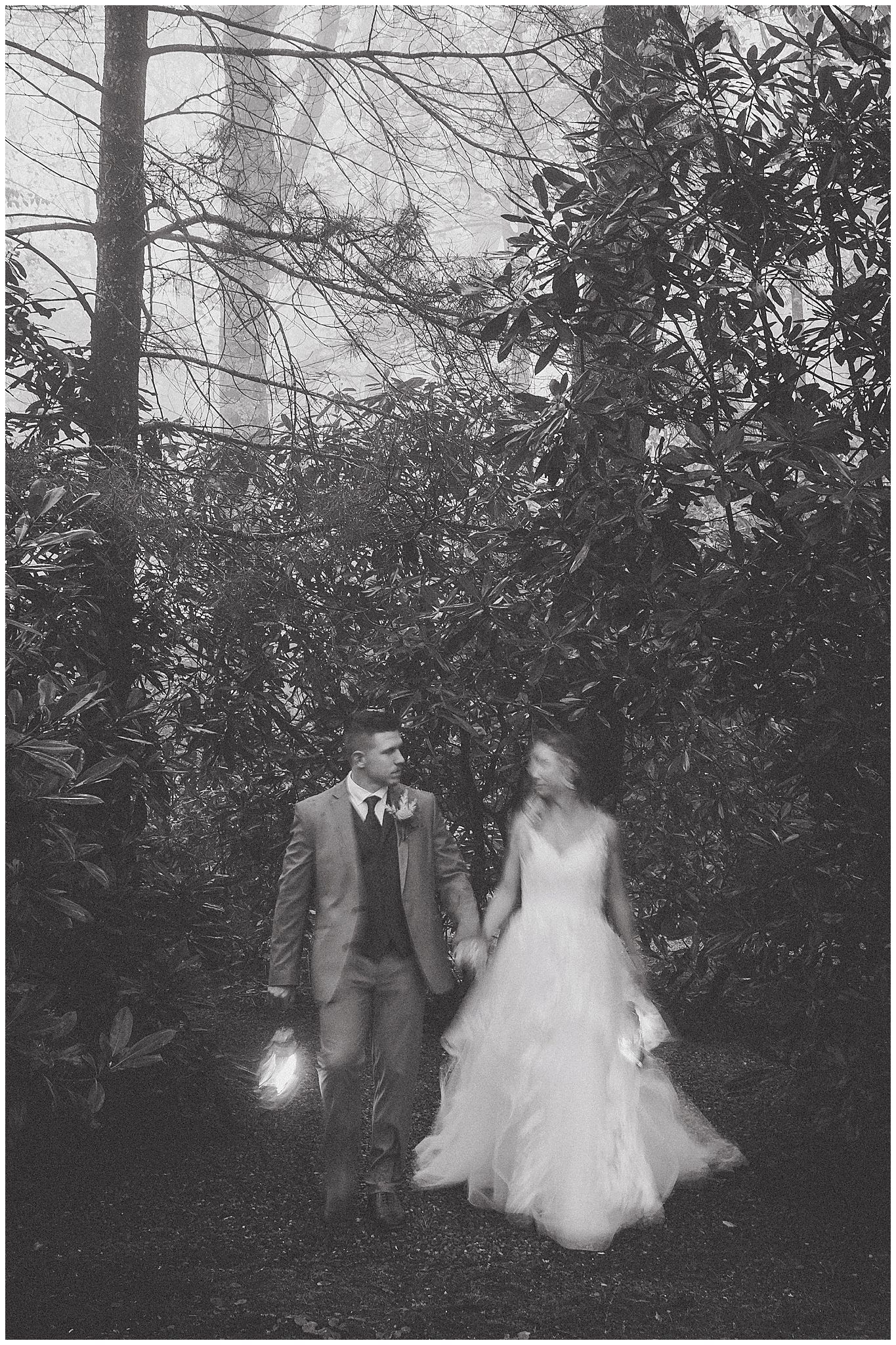 Black and white photo of couple walking through garden path with lush foliage.