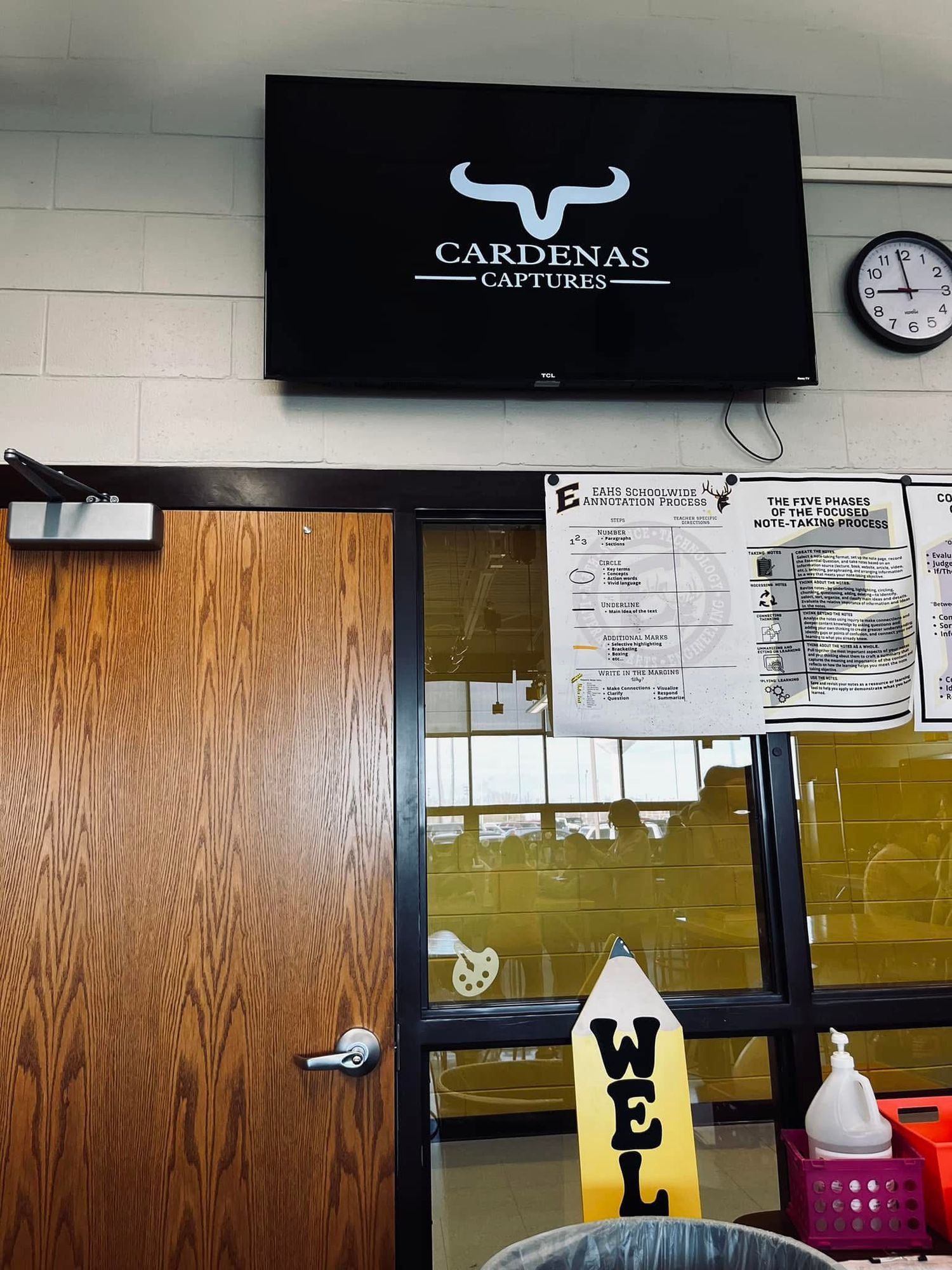 Black office sign displaying 'Cardinals Captures' logo with bull horns mounted on wall above door and bulletin board.
