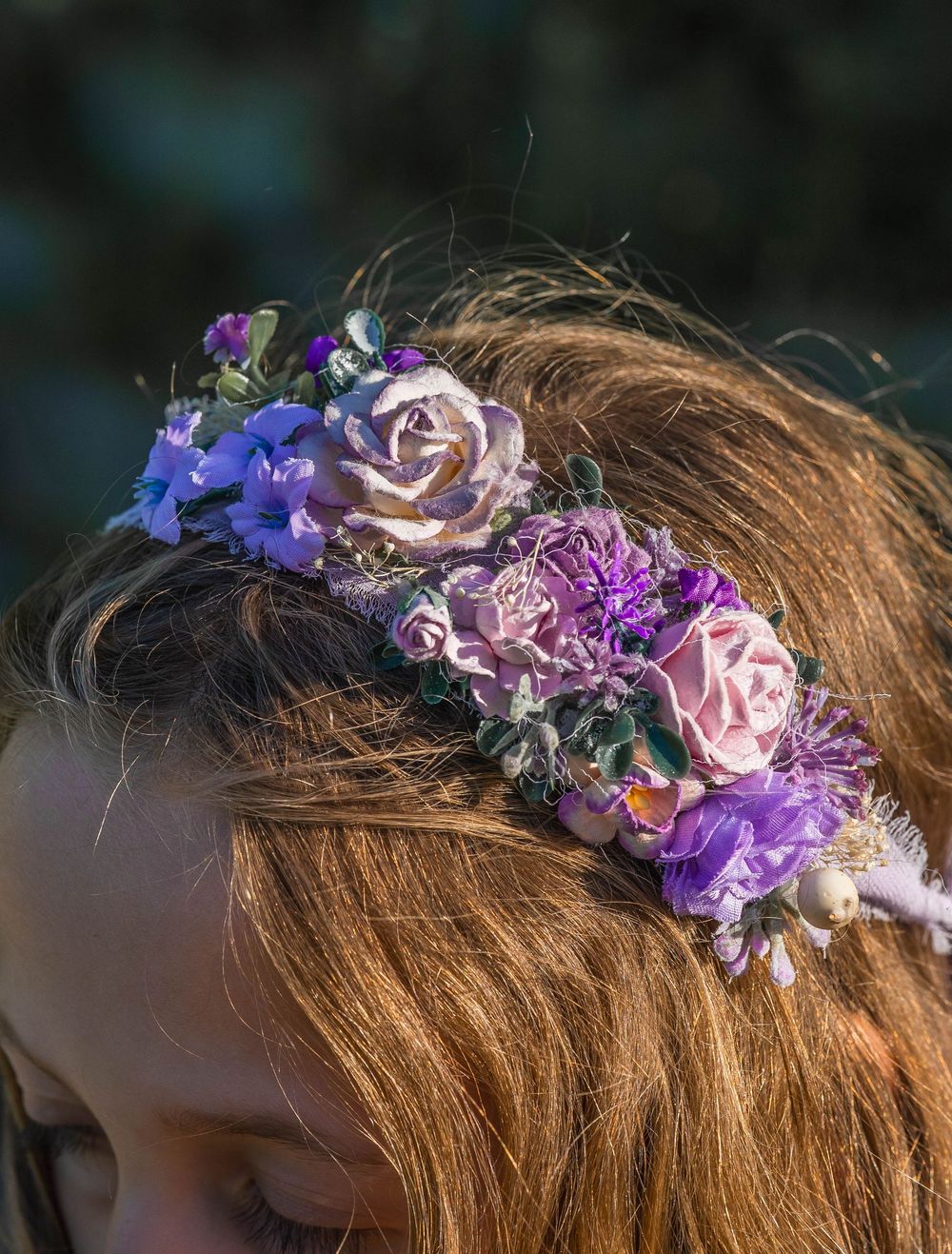 Close-up of a decorative purple and pink floral crown headpiece on a child with auburn hair.