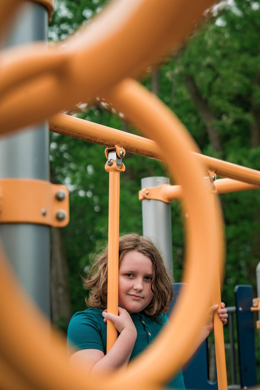 Young boy with wavy hair looking through orange playground equipment bars.