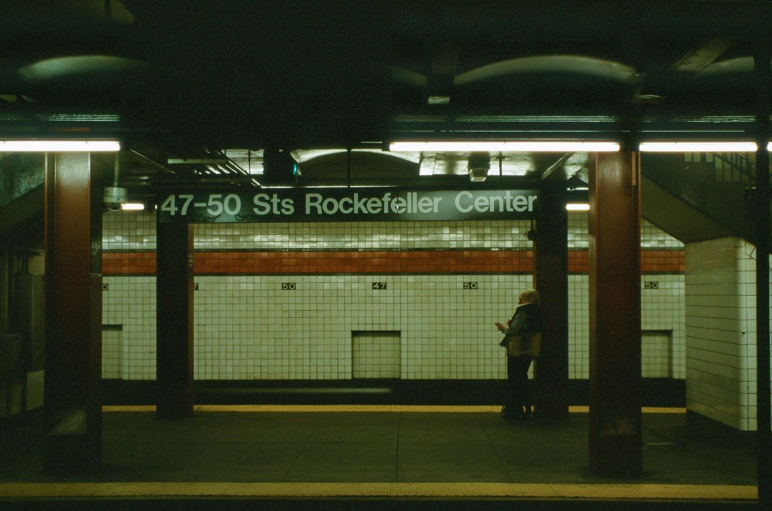 Empty subway platform at 47-50th Street Rockefeller Center station with dark atmospheric lighting.