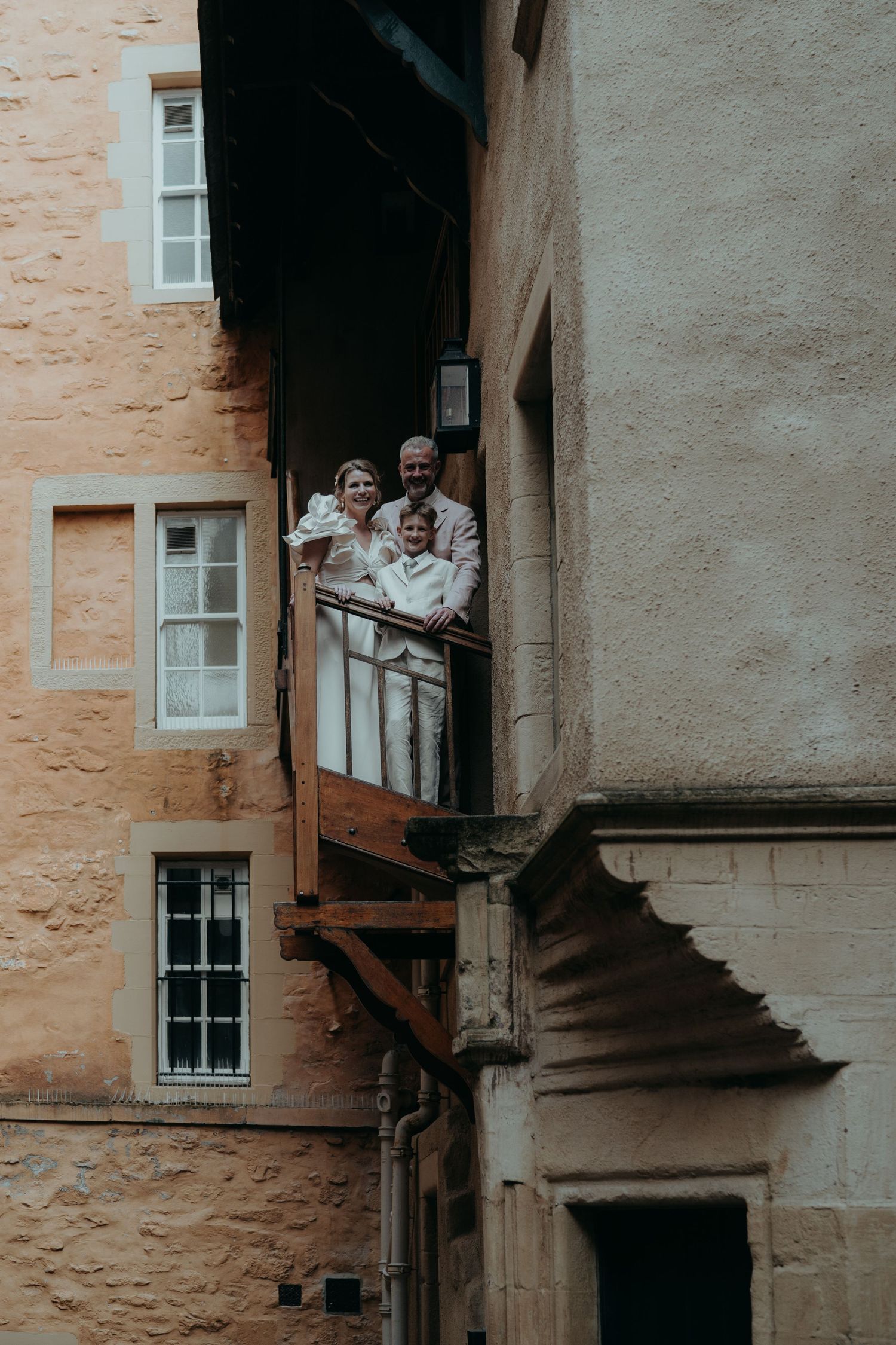 Vintage style photo showing people gathered on a narrow stone balcony between historic buildings.