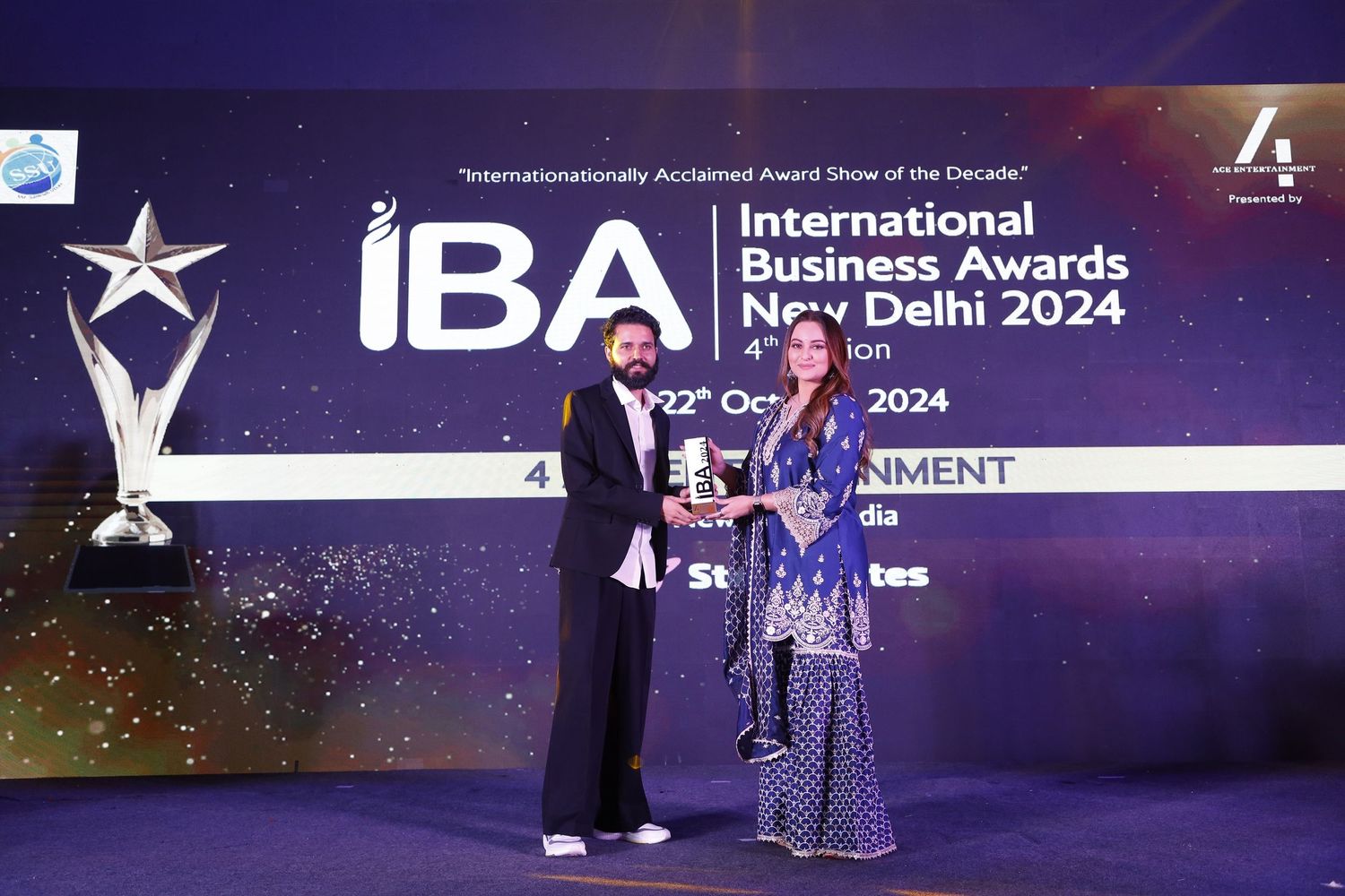 Corporate awards ceremony stage with presenters and star trophy against purple branded backdrop.
