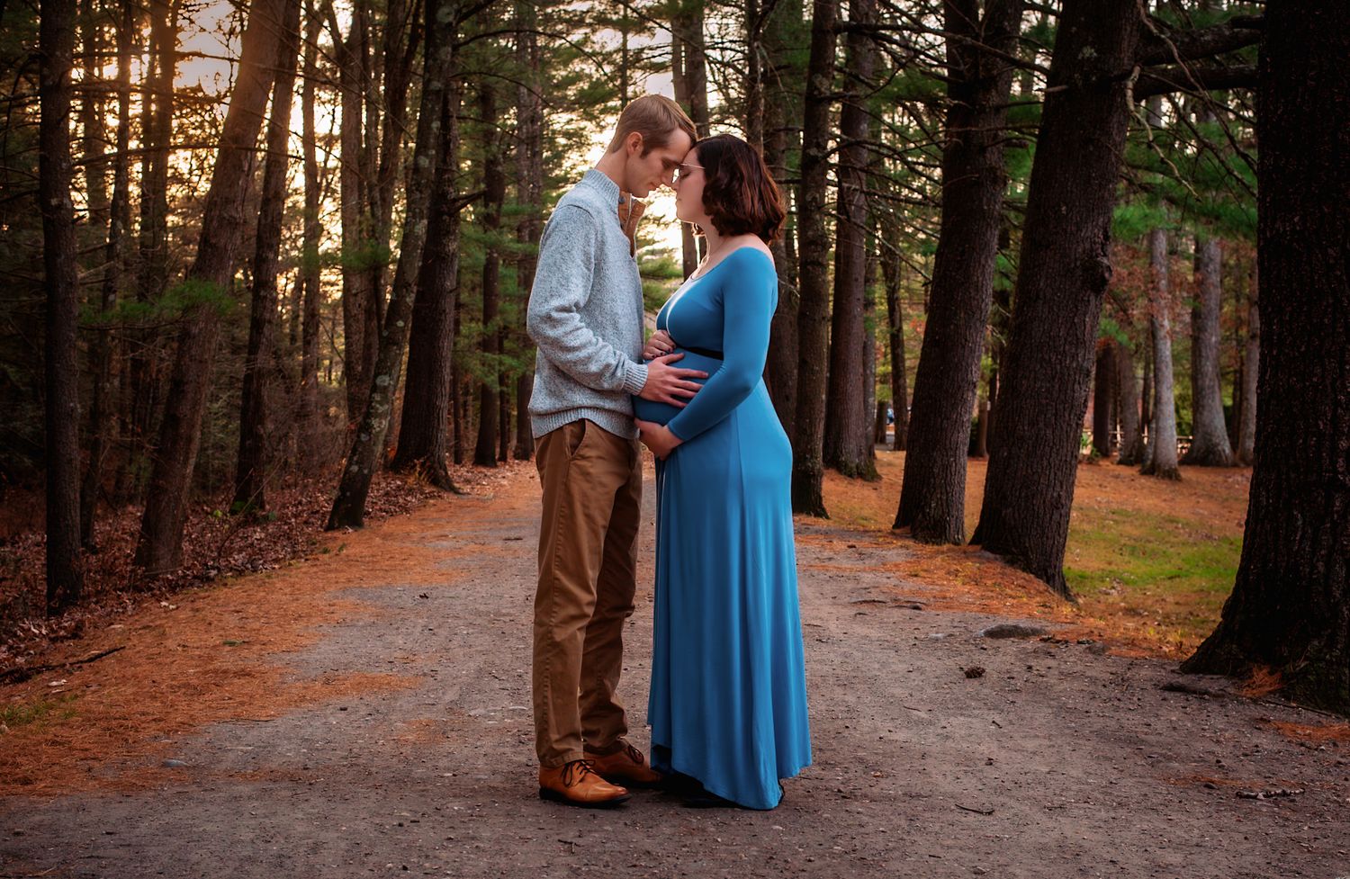 A couple in formal attire walks together along a tree-lined path during autumn.
