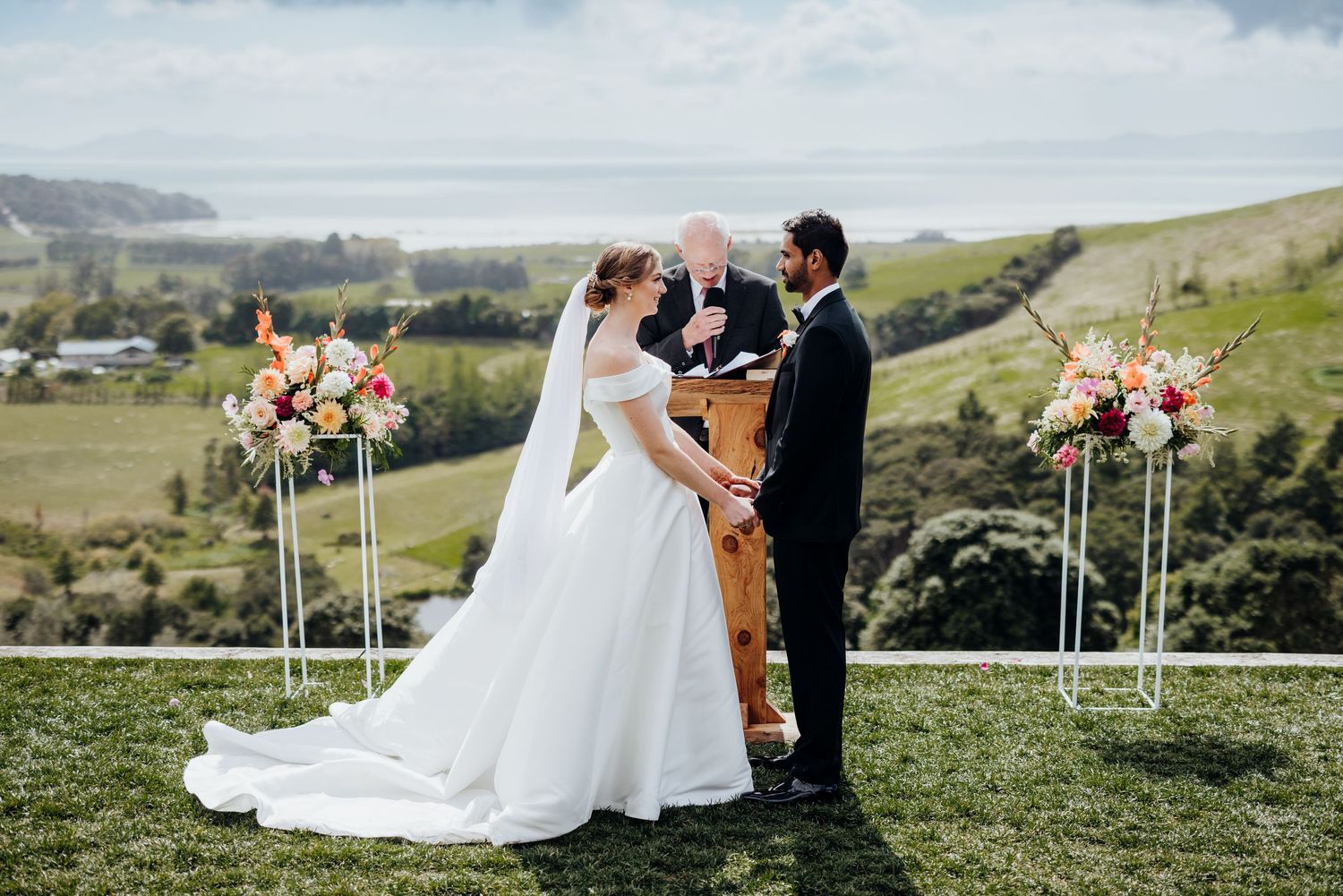 Outdoor wedding ceremony on a hilltop with scenic countryside views and floral arrangements.