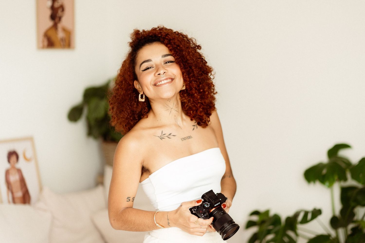 Professional photographer in white dress holding camera in bright interior.