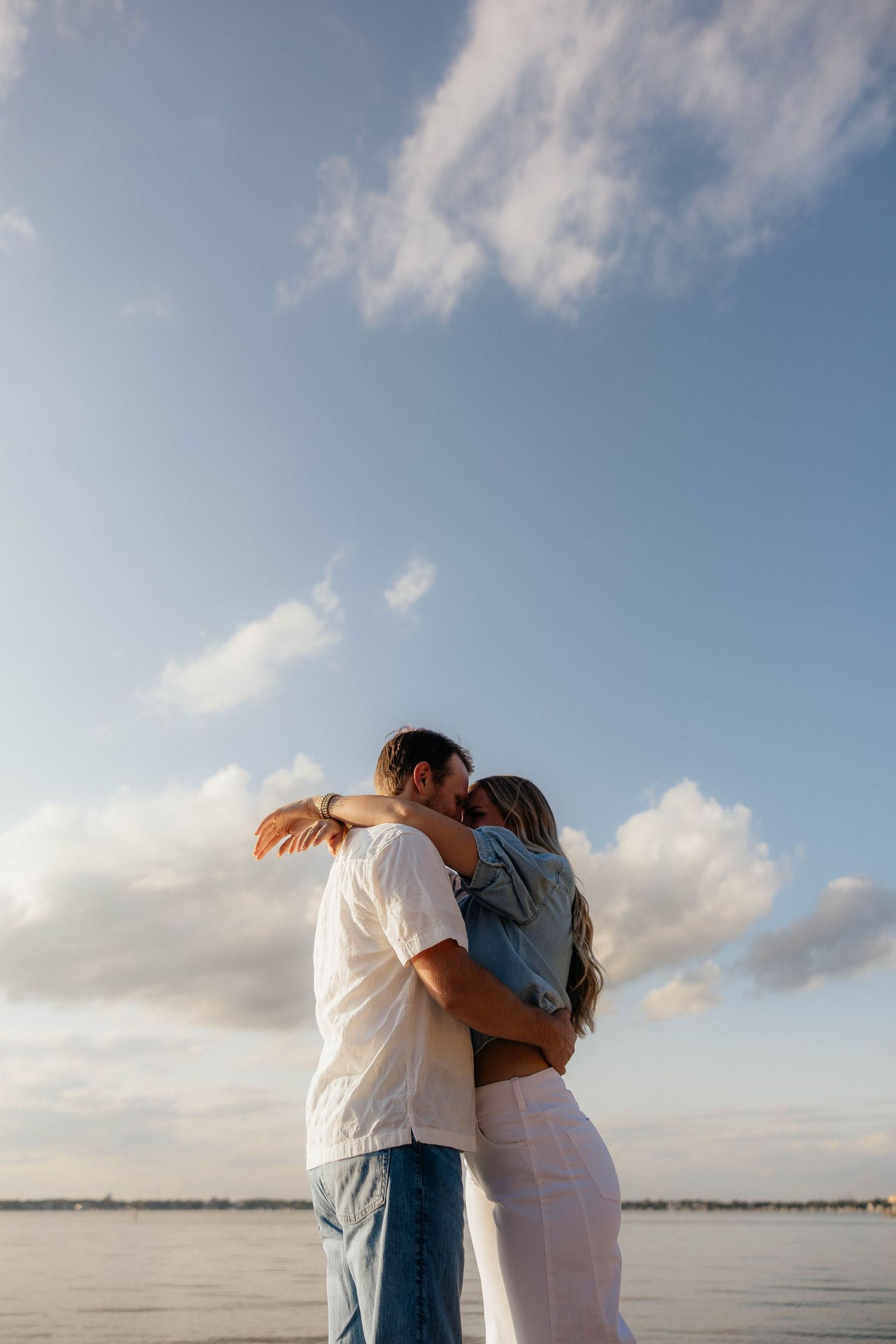 Couple sitting on wooden dock by lake during autumn sunset for engagement session.
