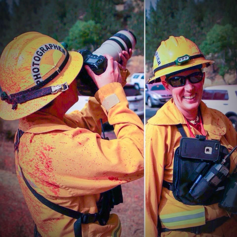 Firefighter photographer in yellow hardhat and gear captures photos with a camera lens at a wildfire scene.