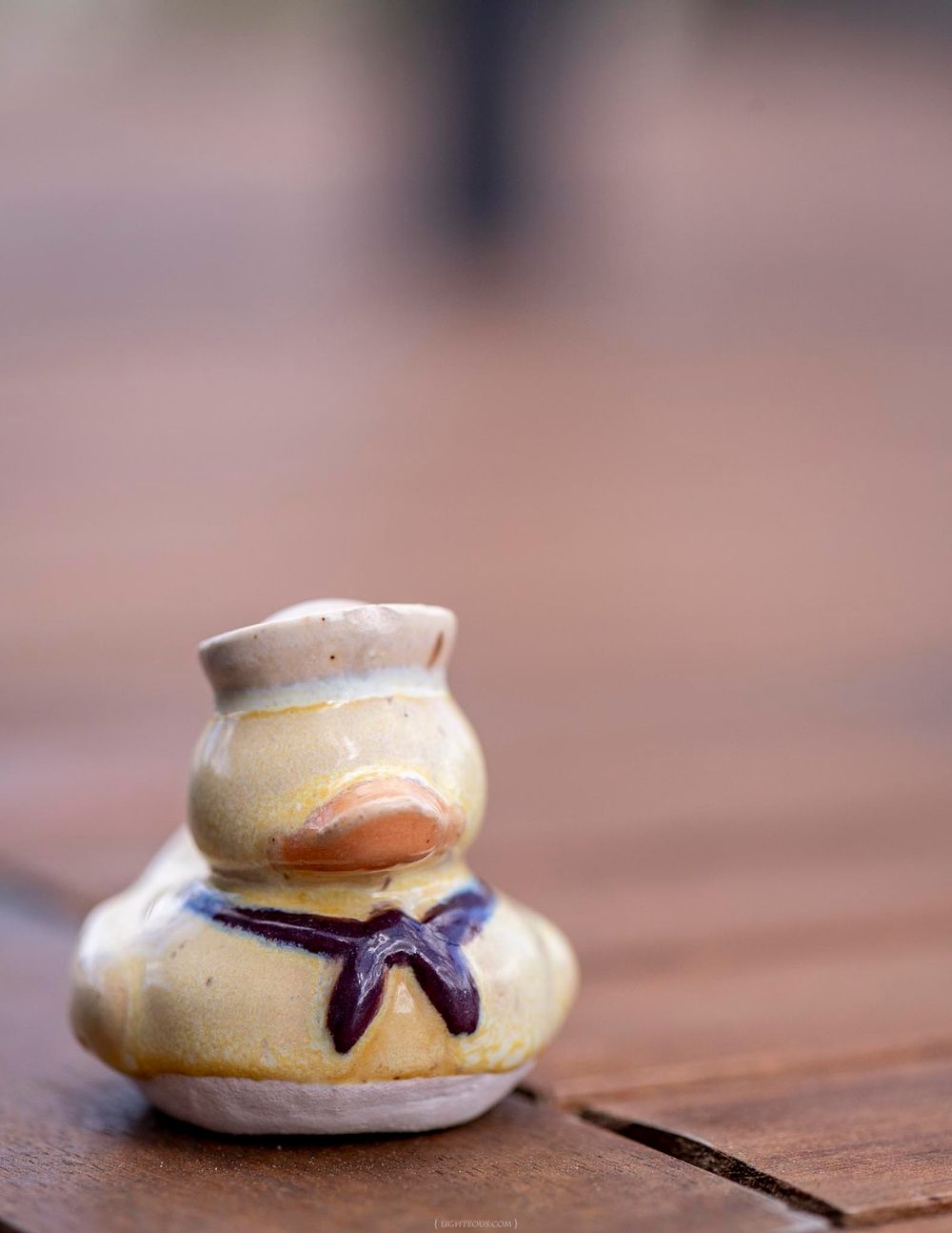 A small ceramic duck figurine with a sailor hat and bow tie sits on a wooden surface.