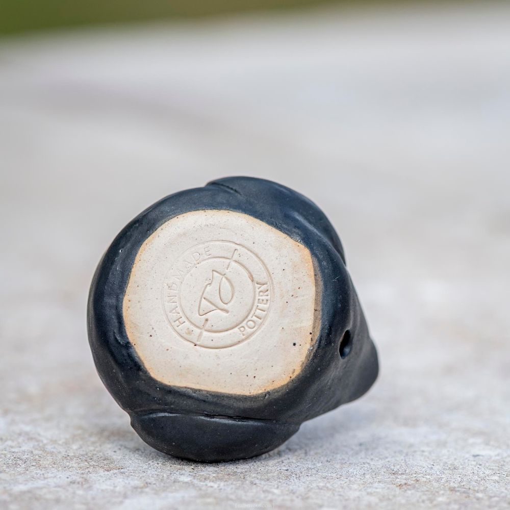 Bottom view of a black glazed ceramic duck showing maker's mark stamp on unglazed base.