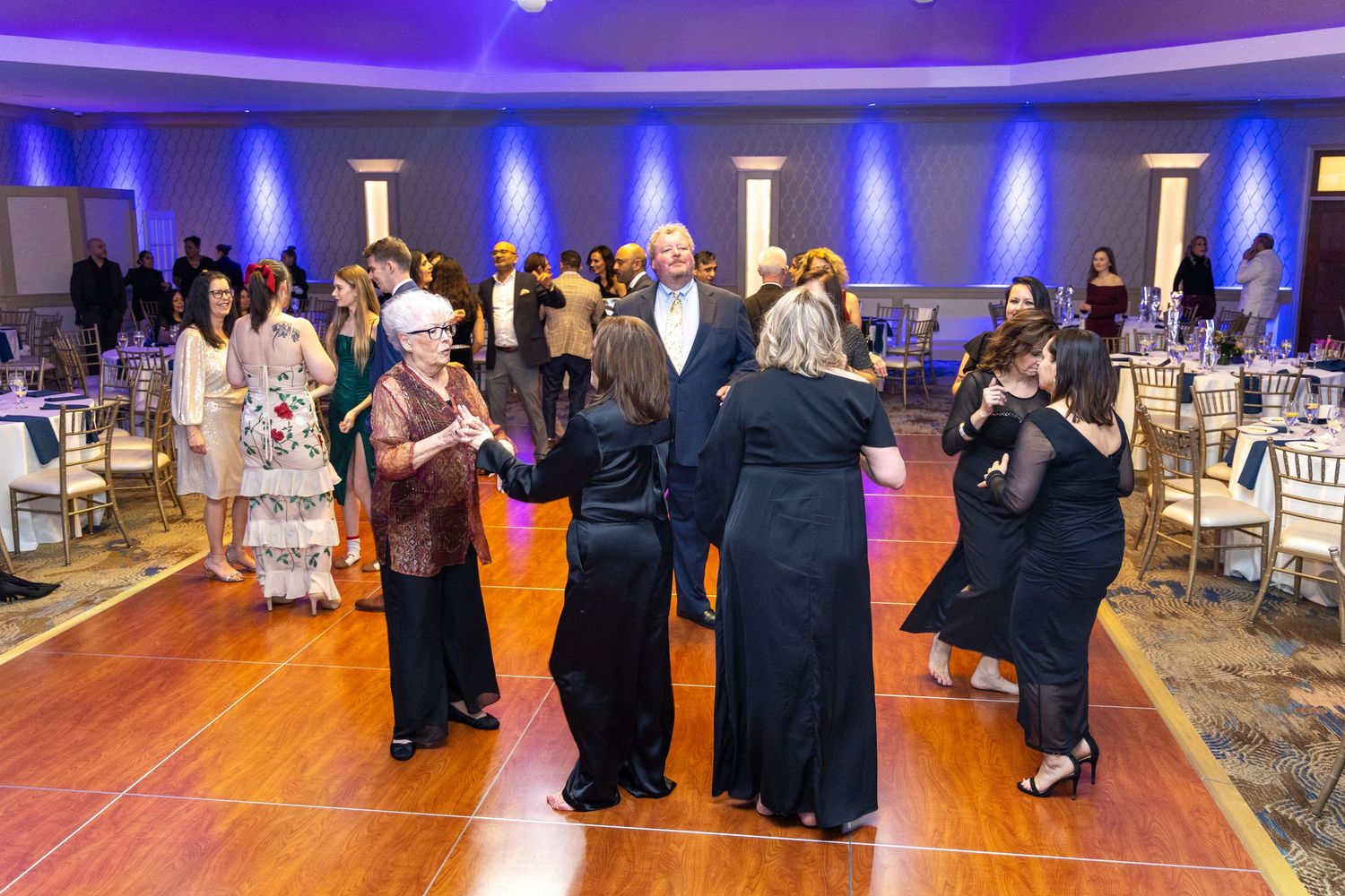 People dancing together on a wooden dance floor at an elegant event with blue lighting and formal attire.
