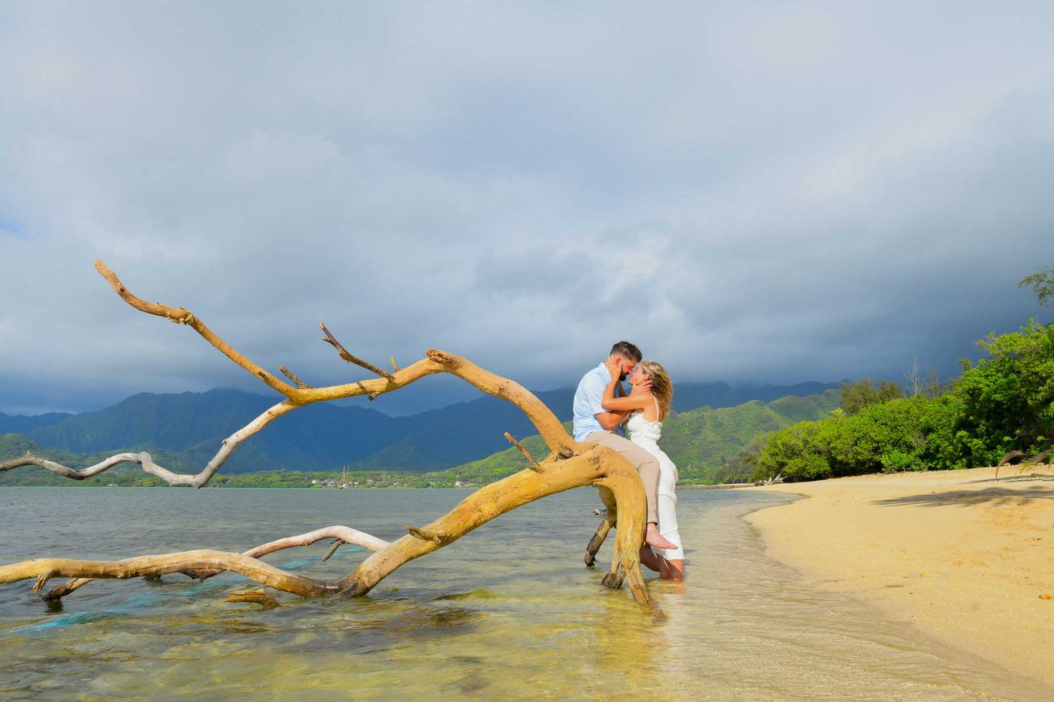 Family photo session in Kualoa regional park in white attire poses joyfully on a scenic beach at sunset with mountains in the background.