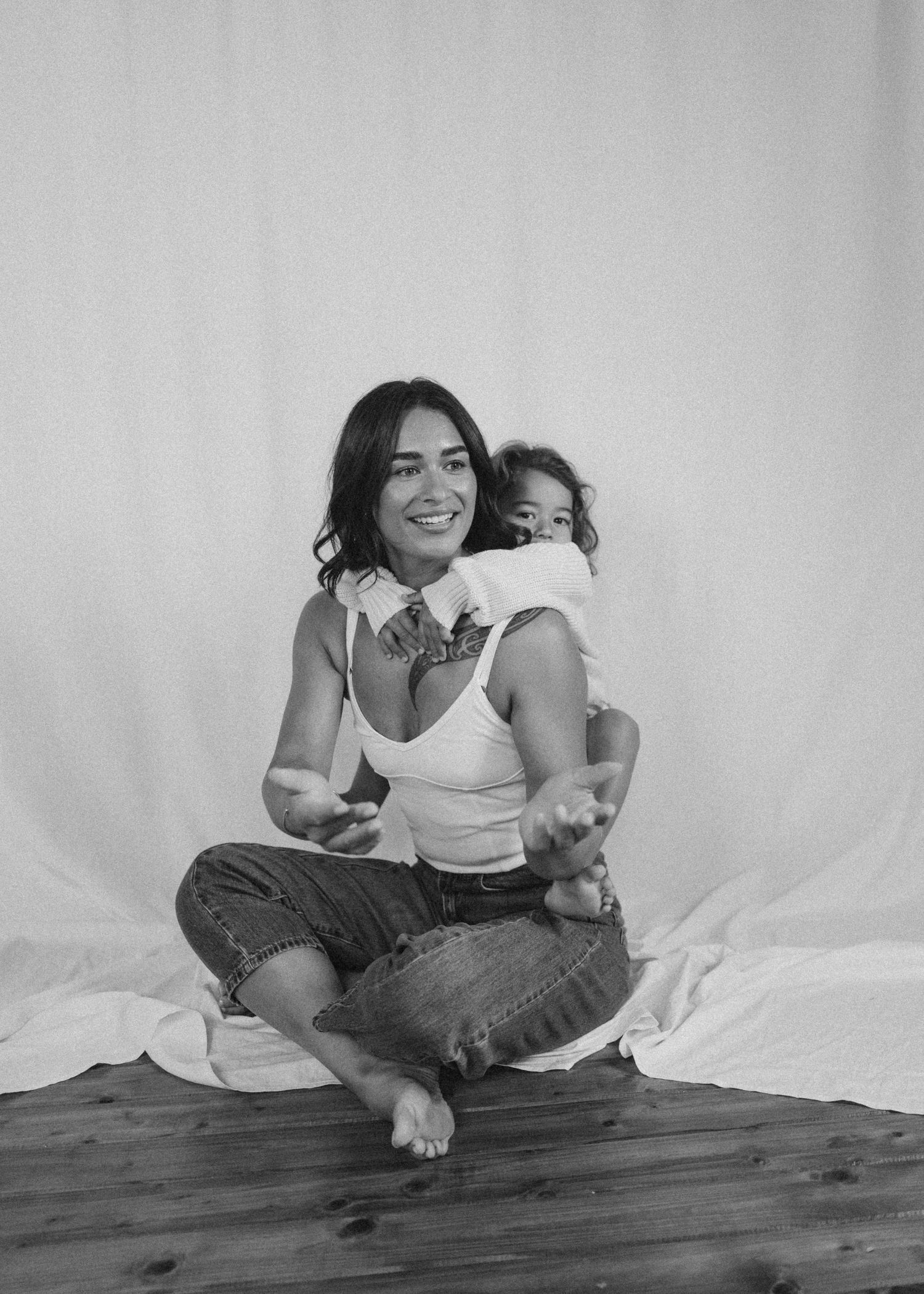 Smiling woman sitting cross-legged with baby on her back, black and white portrait in New Zealand.