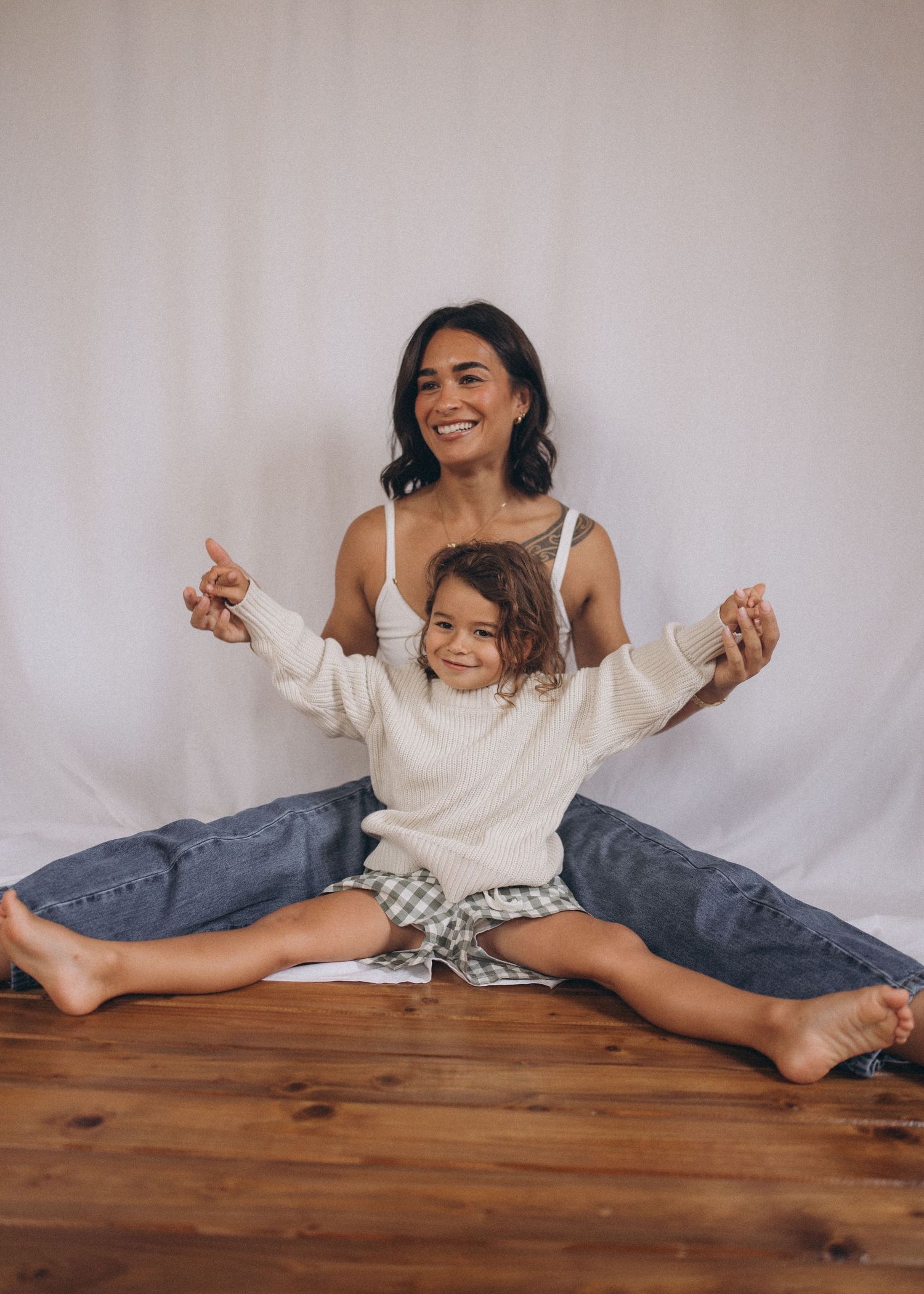 Mother and young child sitting together on wood floor, child spreading arms wide in New Zealand.