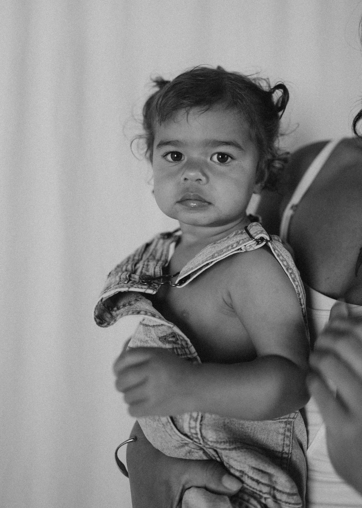 Close-up black and white portrait of a baby in denim overalls being held in New Zealand.