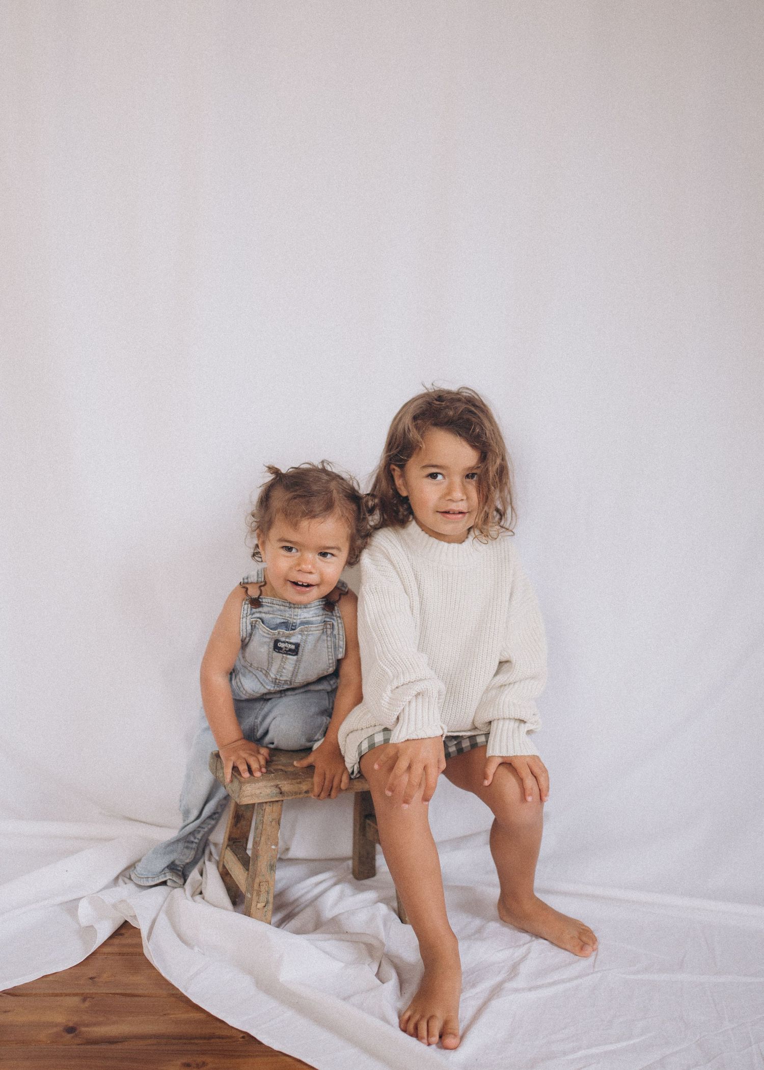 Two young children posing together on wooden stool against white backdrop in New Zealand.